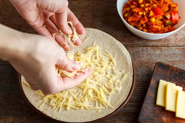 Foto una mujer asperja un pastel de queso para la tortilla de quesadilla. fabricación de quesadilla a domicilio.