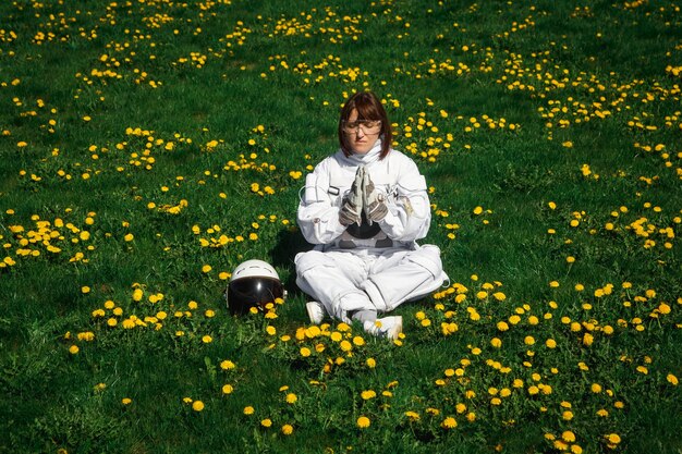 Mujer astronauta sin casco se sienta en un césped verde en una posición meditativa