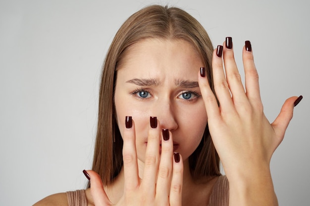 Mujer asustada cubriendo su cara con las manos sobre un fondo gris