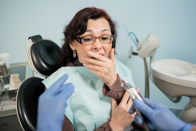 Mujer asustada por los dentistas y cubriéndose la boca con la mano en la cita con el dentista en la clínica dental