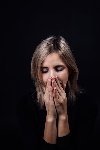 Mujer asustada con las manos ocultando la nariz y la boca en silencio vestida con una blusa negra sobre fondo negro Víctima de abuso físico y psicológico Gaslighting Agresión relativa