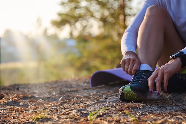 Foto la mujer se ata los cordones de los zapatos en las zapatillas de deporte al aire libre bajo los rayos del sol concepto de deportes y un estilo de vida saludable