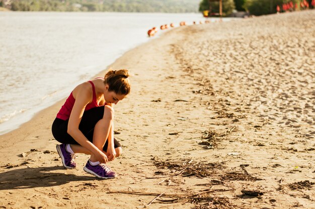 Mujer atarse los zapatos deportivos y prepararse para correr y hacer ejercicio en la playa en verano