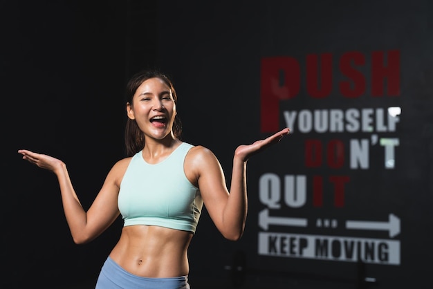 Mujer atleta asiática sonriente en ropa deportiva cuerpo musculoso delgado posando acción después del ejercicio en el gimnasio