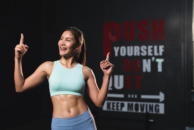 Mujer atleta asiática sonriente en ropa deportiva cuerpo musculoso delgado posando acción después del ejercicio en el gimnasio