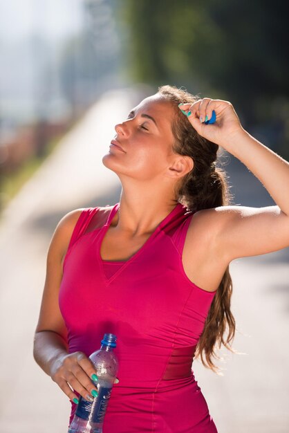 Foto mujer atleta bebiendo agua de una botella después de trotar en la ciudad en un día soleado