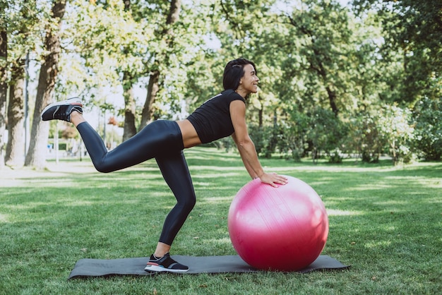 Mujer atleta con una gran pelota de fitness entrena en el parque