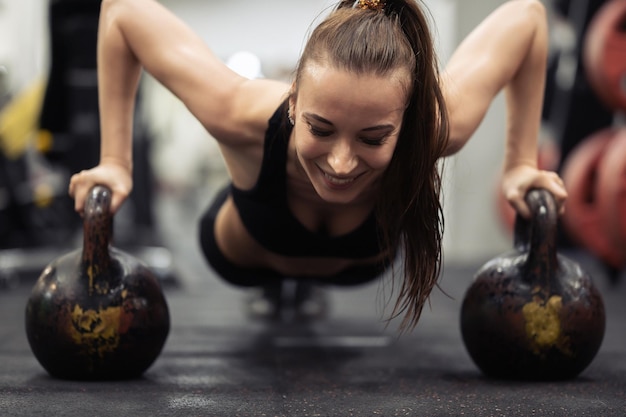 Foto mujer atleta haciendo flexiones en dos pesas rusas