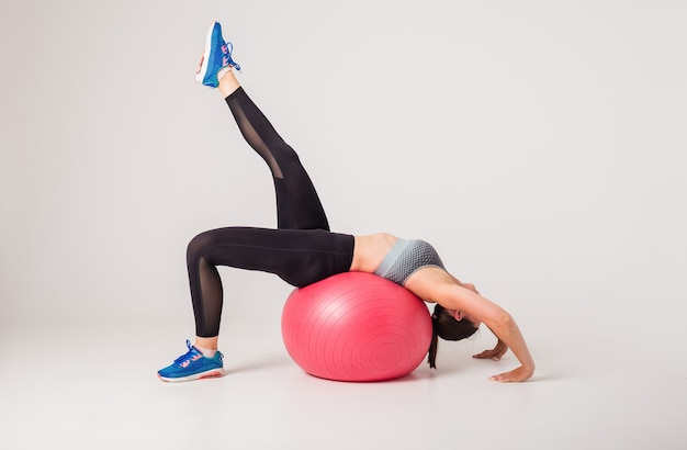 Mujer atleta realiza ejercicios en una pelota de fitness en un blanco aislado con espacio para texto