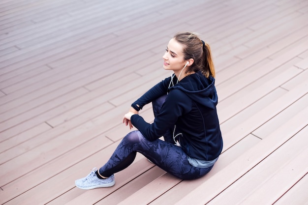 Mujer atleta sentada en las escaleras mientras escucha música durante el ejercicio de trotar