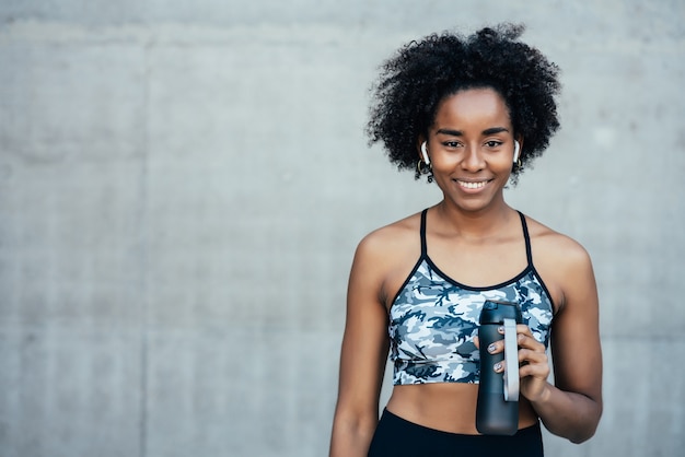 Mujer atlética afro bebiendo agua y relajarse después de hacer ejercicio al aire libre. Deporte y estilo de vida saludable.