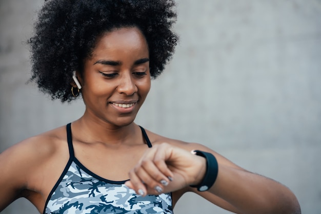 Mujer atlética afro que controla el tiempo en su reloj inteligente mientras hace ejercicio al aire libre. Concepto de deporte y estilo de vida saludable.