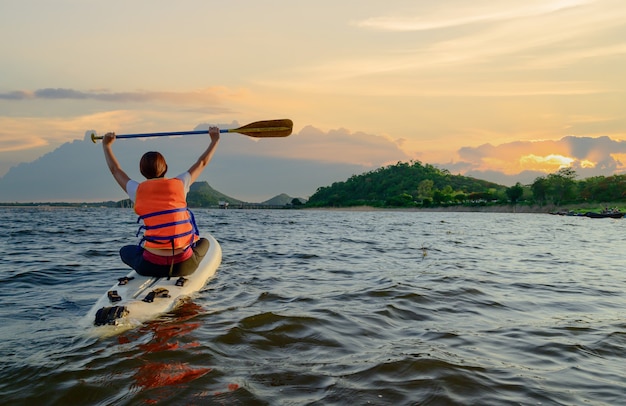 Mujer atlética asiática en stand paddle board en el lago. Actividad de SUP al aire libre en solitario y deporte acuático en vacaciones de verano.