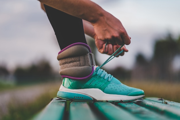 Foto mujer atlética atar cordones de los zapatos en las zapatillas mientras camina con pesas durante el entrenamiento al aire libre.