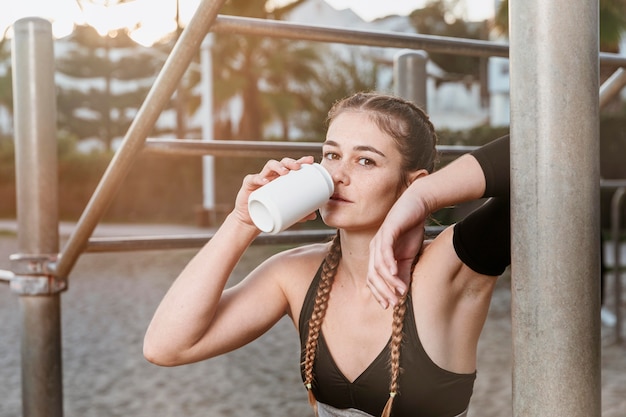 Mujer atlética bebiendo refrescos después de hacer ejercicio en la playa