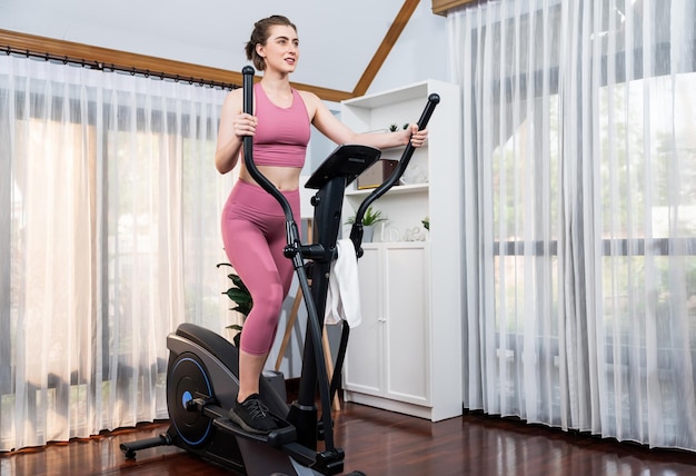 Mujer atlética y deportiva corriendo en una máquina elíptica en el hogar de gaiety