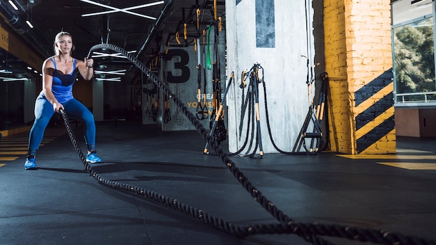 Una mujer atlética ejercita ingenio cuerdas de batalla en el gimnasio