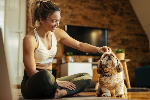 Mujer atlética feliz divirtiéndose mientras abraza a su perro en casa.