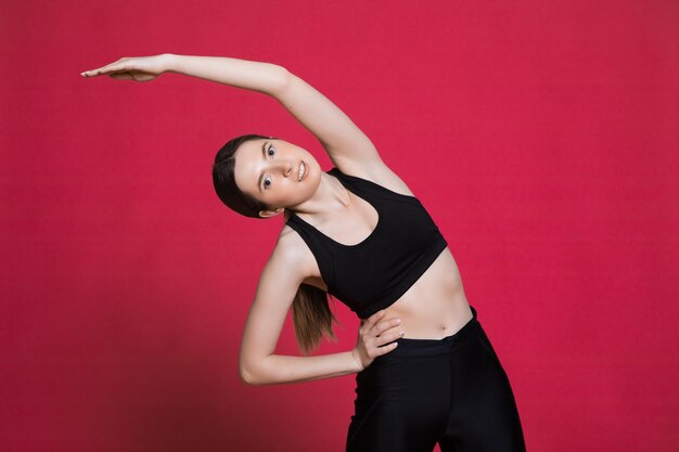 Mujer atlética feliz Foto de mujer deportiva en ropa deportiva negra de moda sobre fondo rojo