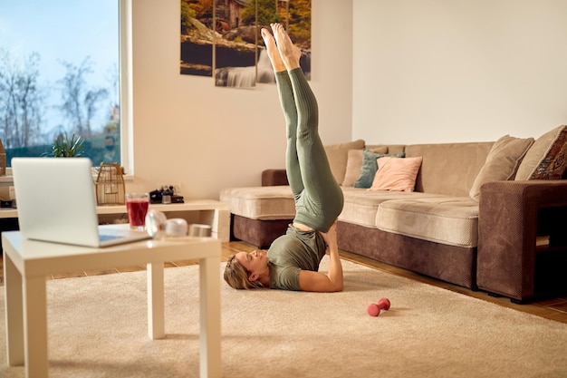 Mujer atlética feliz en pose de hombro apoyada haciendo ejercicio en la sala de estar