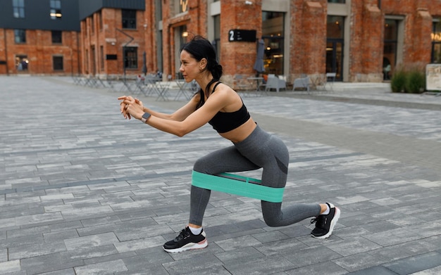 Mujer atlética haciendo ejercicio de estocadas con una banda elástica de fitness al aire libre