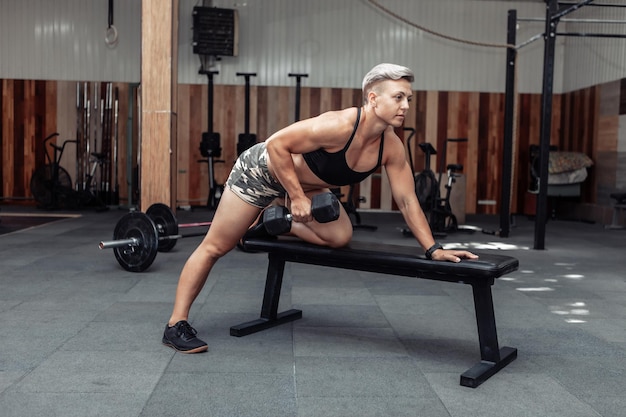 Mujer atlética haciendo ejercicio de fila con mancuernas con una mano. Entrenamiento muscular de la espalda. Culturismo y Fitness