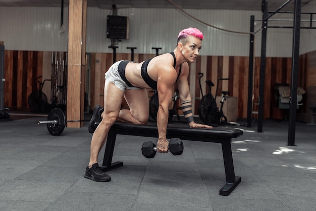 Mujer atlética haciendo ejercicio de fila con mancuernas con una mano. Entrenamiento muscular de la espalda. Culturismo y Fitness