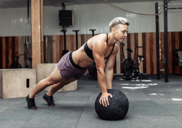 Mujer atlética muscular empuja con balones medicinales en un gimnasio moderno. Cross fit, entrenamiento funcional