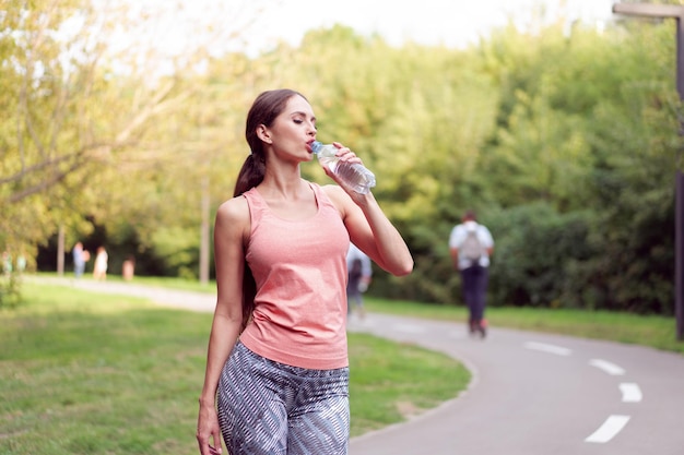 Mujer atlética de pie pista de atletismo en el parque de verano beber agua después de correr ejercicios Entrenamiento matutino femenino caucásico Jogging Concepto de estilo de vida saludable Entrenamiento cardiovascular lanzamiento medio