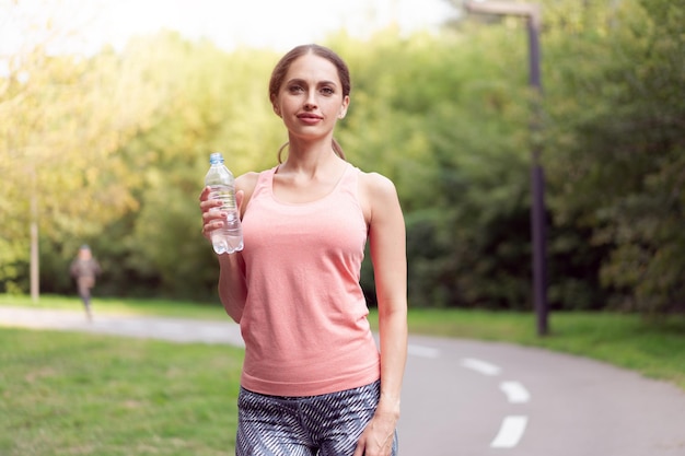 Mujer atlética de pie pista de atletismo en el parque de verano sosteniendo una botella de agua después de correr ejercicios Entrenamiento matutino de mujeres caucásicas Jogging Concepto de estilo de vida saludable Entrenamiento cardiovascular lanzamiento medio