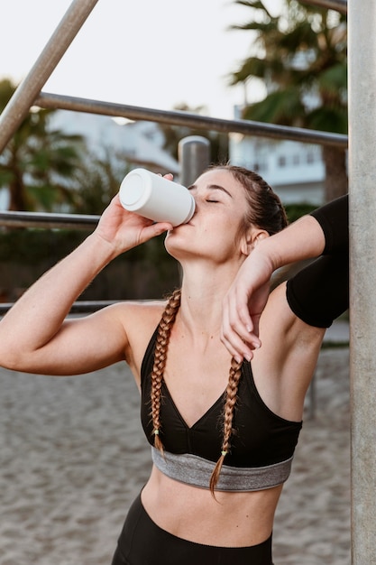 Foto mujer atlética en la playa bebiendo refrescos después de hacer ejercicio