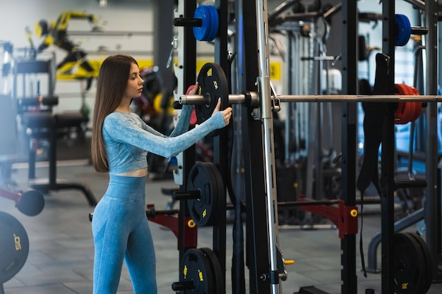 Mujer atlética pone el disco en la máquina Smith Chica haciendo ejercicio en el gimnasio