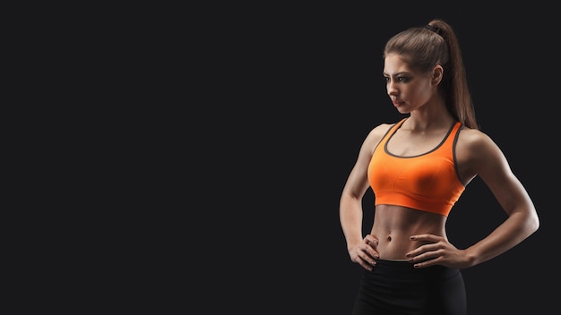 Mujer atlética posando en estudio, culturista. Cuerpo musculoso y músculos fuertes. Filmada sobre fondo negro, bajo perfil. Concepto de culturismo, espacio de copia