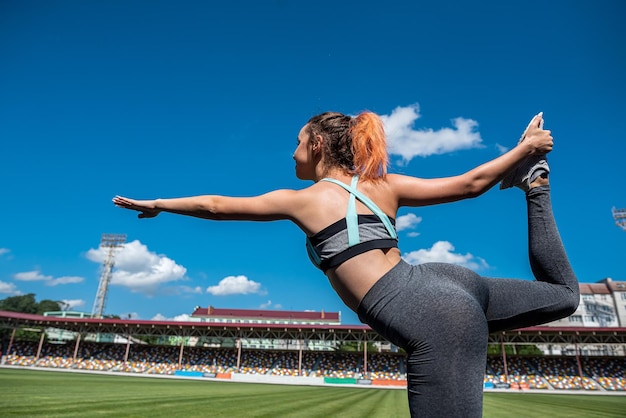 Mujer atlética practicando pose de yoga en el estadio con hierba verde