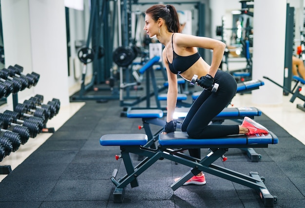 Mujer atlética que bombea los músculos con pesas. Concepto de deporte, fitness y estilo de vida saludable.