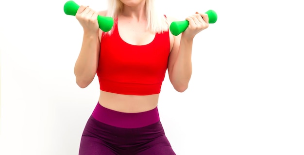 Mujer atlética que bombea los músculos con pesas sobre fondo gris