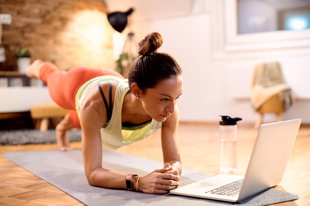 Mujer atlética que tiene clase de ejercicio en línea mientras usa una computadora portátil en casa