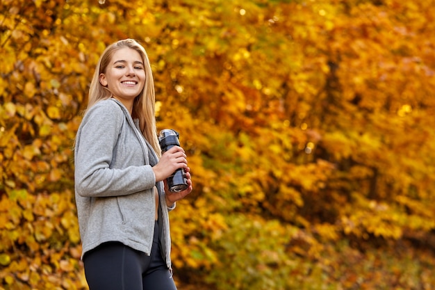 Mujer atlética sosteniendo una botella de agua limpia en el bosque de otoño