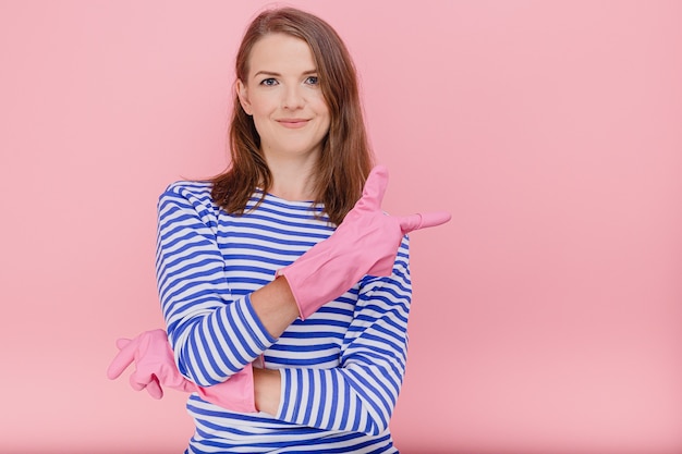 Mujer atractiva ama de casa usa guantes de limpieza de goma y un suéter de rayas azul casual