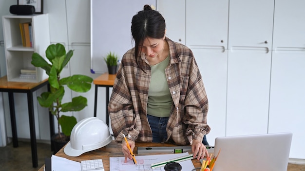 Mujer atractiva arquitecto examinando planos para un nuevo proyecto en su lugar de trabajo.