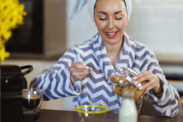 Una mujer atractiva en bata de baño preparando un cereal para el desayuno y teniendo un ritual de placer matutino en casa.