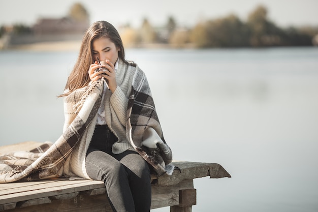 Mujer atractiva bebiendo café o té en el muelle al aire libre