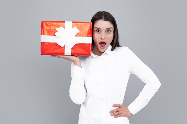 Mujer atractiva con caja presente posando con expresión de cara sorprendida sobre fondo gris Expresiones faciales expresivas con cara sorprendida Día de San Valentín cumpleaños feliz año nuevo regalo personas concepto