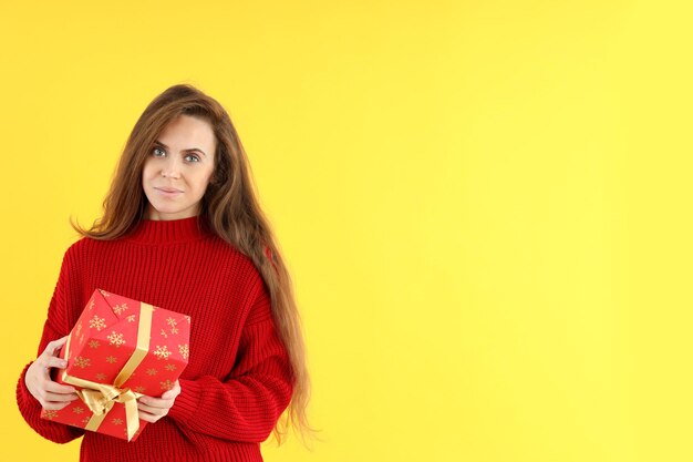 Mujer atractiva con caja de regalo de Navidad sobre fondo amarillo