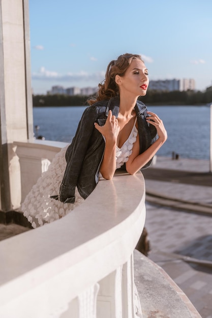 Una mujer atractiva celebra la vida con un vestido blanco de verano y una chaqueta vaquera.