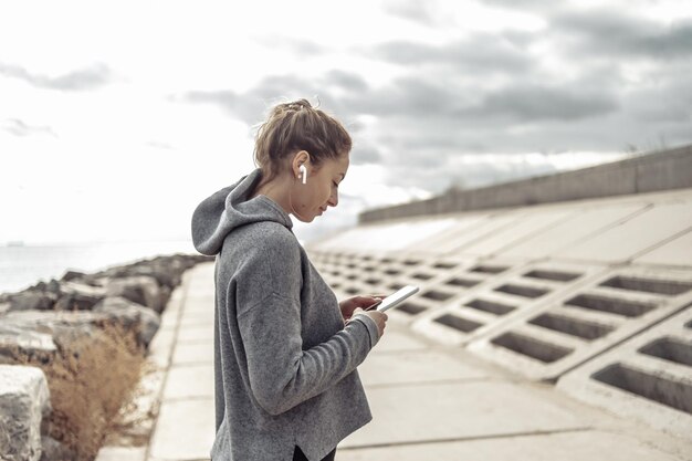 Mujer atractiva deportiva usando teléfono inteligente y escuchando música en auriculares al aire libre