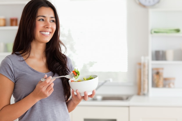 Mujer atractiva disfrutando de un plato de ensalada mientras está de pie