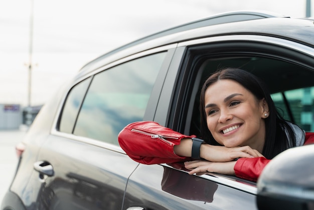 Foto mujer atractiva está disfrutando de su viaje. ella está sentada en el asiento del pasajero en el auto y sonriendo. lady está mirando por la ventana y soñando.