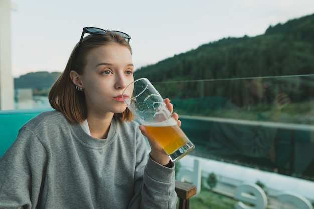 Mujer atractiva disfrutando de un vaso de cerveza en un paisaje de bosques y lagos