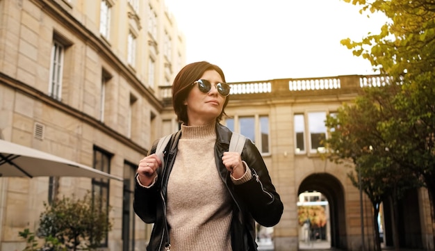 Una mujer atractiva y elegante con gafas de sol camina por la calle de la ciudad con una mochila